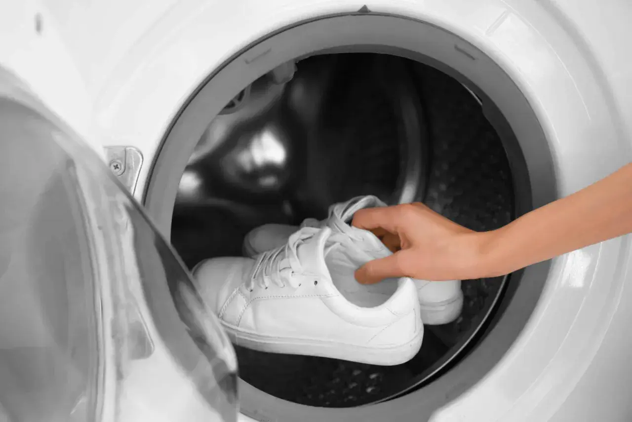 Weiße Sneaker werden in eine Waschmaschine gelegt.
