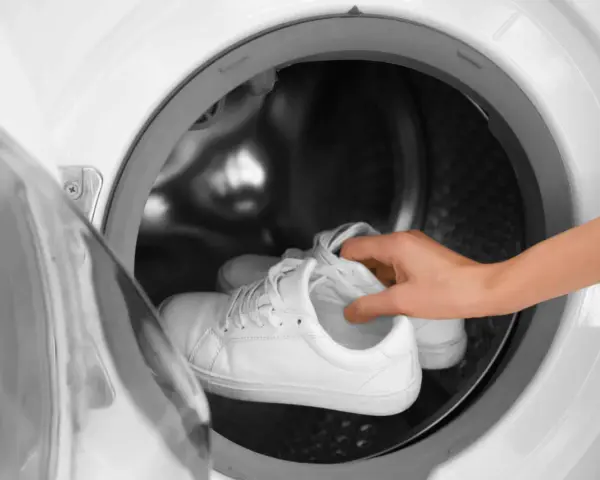 Weiße Sneaker werden in eine Waschmaschine gelegt.
