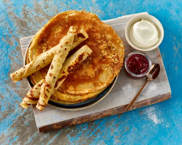 Ein Stapel goldbrauner Pfannkuchen, einige gerollt, mit Marmelade und Sahne. Ein einfaches Pfannkuchen Rezept für jeden Tag.