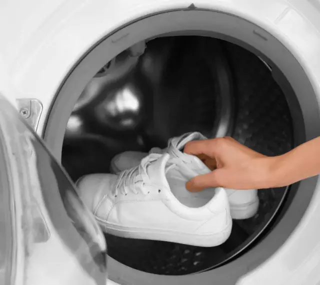 Weiße Sneaker werden in eine Waschmaschine gelegt.