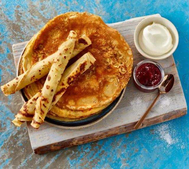 Ein Stapel goldbrauner Pfannkuchen, einige gerollt, mit Marmelade und Sahne. Ein einfaches Pfannkuchen Rezept für jeden Tag.