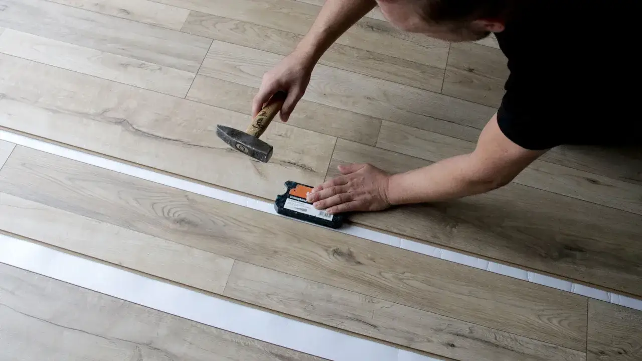 Mann verlegt Laminat mit Hammer und Schlagklotz. Die neuen Dielen werden präzise zusammengefügt.