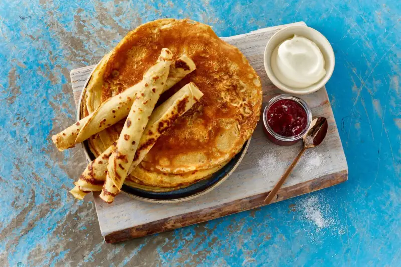 Ein Stapel goldbrauner Pfannkuchen, einige gerollt, mit Marmelade und Sahne. Ein einfaches Pfannkuchen Rezept für jeden Tag.